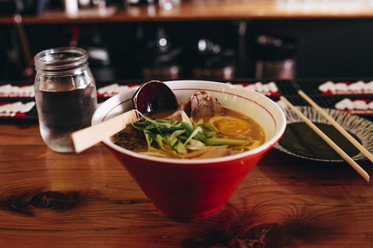 A bowl of ramen sitting on top of a red bartop in a ramen Denver restaurant