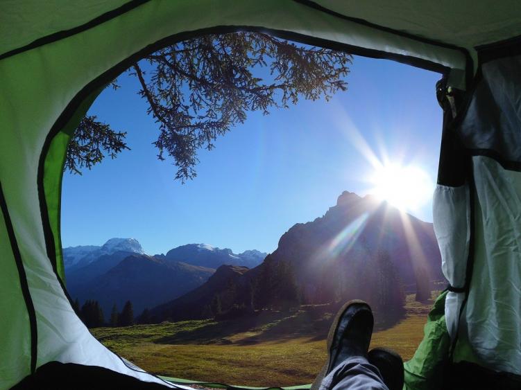 A person relaxing in their tent at a free campsite in Colorado, with the tent door open and the sun shining in behind the mountains