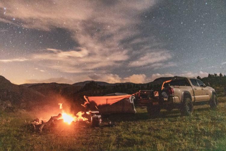 A tan pickup truck, tent, and campfire under a night sky at one of the best free campsites in Colorado