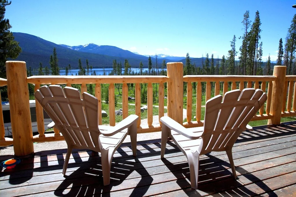 Two Adirondack chairs on a deck facing a lake and mountains at one of many secluded cabins in Colorado