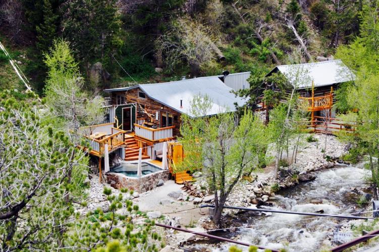 Two cabins in the woods surrounded by trees, one with a private hot springs tub