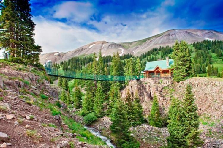 A suspension bridge over a creek leading to one of the most secluded cabins in Colorado, against the mountains and sky