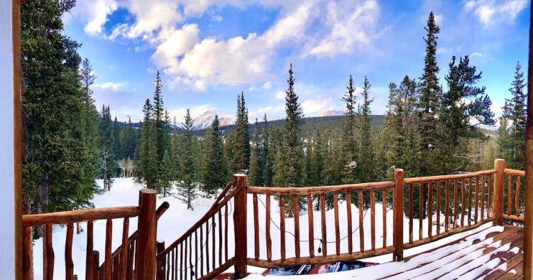 A snow-covered wooden deck looking out at mountains at one of the most secluded cabins in Colorado