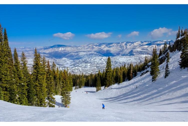 A few skiers going down a slope with mountains in the background of Colorado ski season