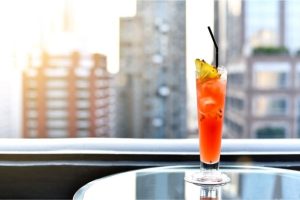A red-colored cocktail with a city view in the background at a rooftop bar in Denver