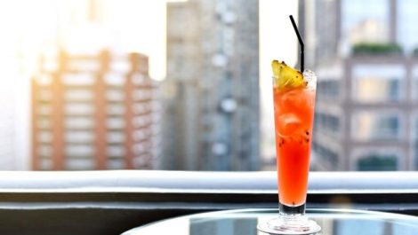 A red-colored cocktail with a city view in the background at a rooftop bar in Denver