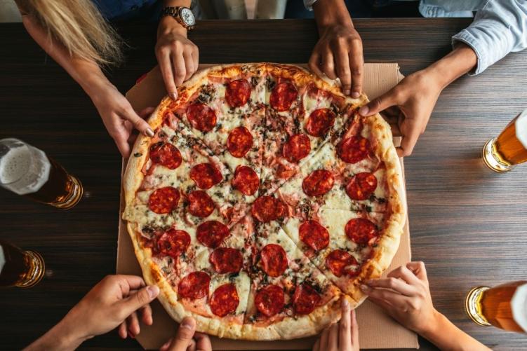 Several people gathered around a pizza, reaching for a slice at one of the best pizza places in Denver